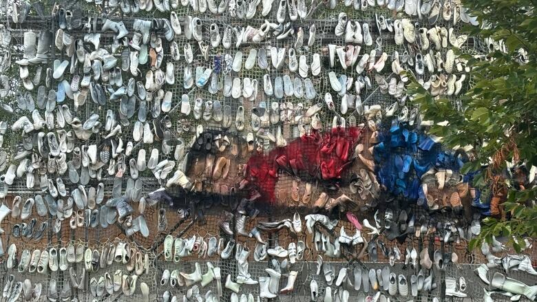 Shoes arranged on an tall outdoor display, some in the shape of a body lying flat. 