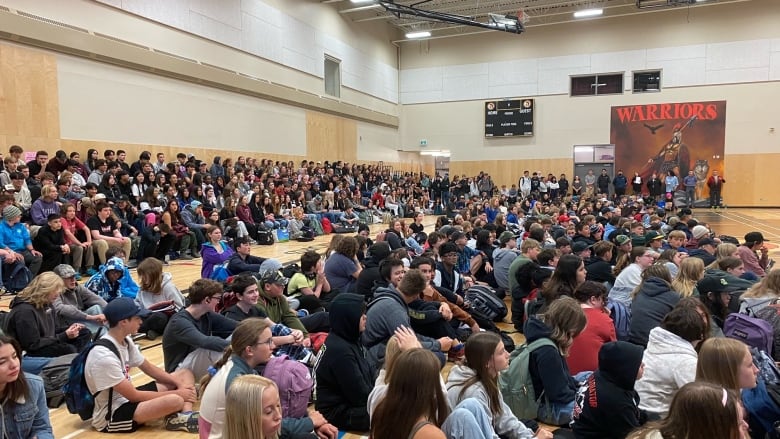 Many students sitting around with a Warriors sign in the background.