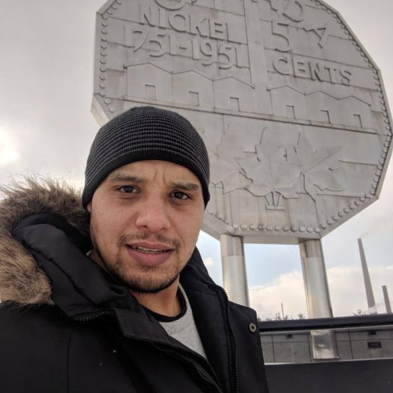 A man wearing a black hat with a big nickel in the background.