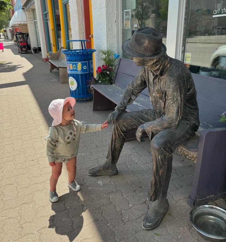 A child holds the hand of a statue sitting on a bench 