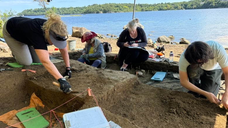 Archaeologists dig along the shores of a river on a sunny summer day.