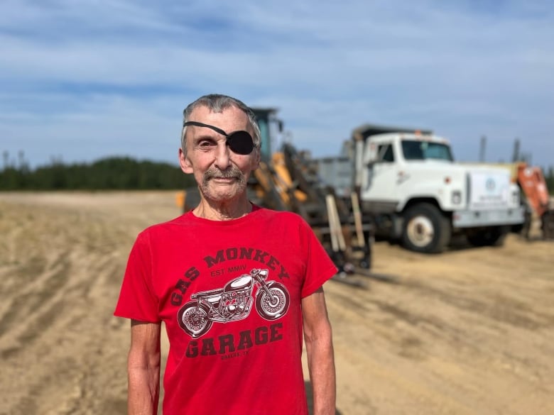 A man with an eyepatch wearing a red t-shirt stands on a construction site.