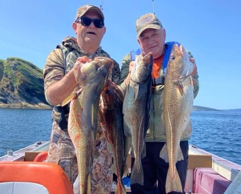 Two men stand in a boat, holding up freshly caught fish.