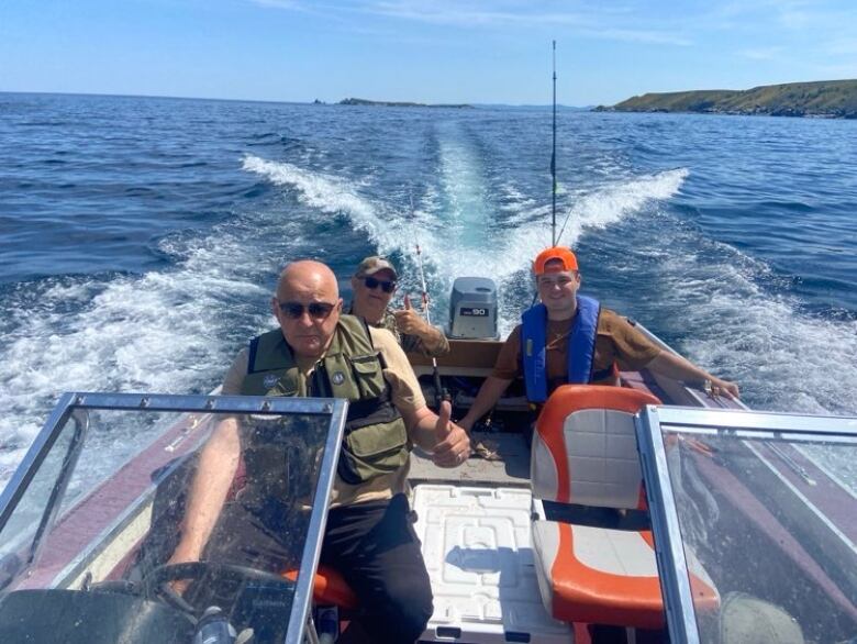 Three men sit in a motorboat making its way through the water. Two of them are giving the thumbs-up.