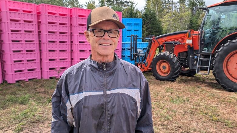 A man stands in front of some brightly coloured bins for collecting blueberries  