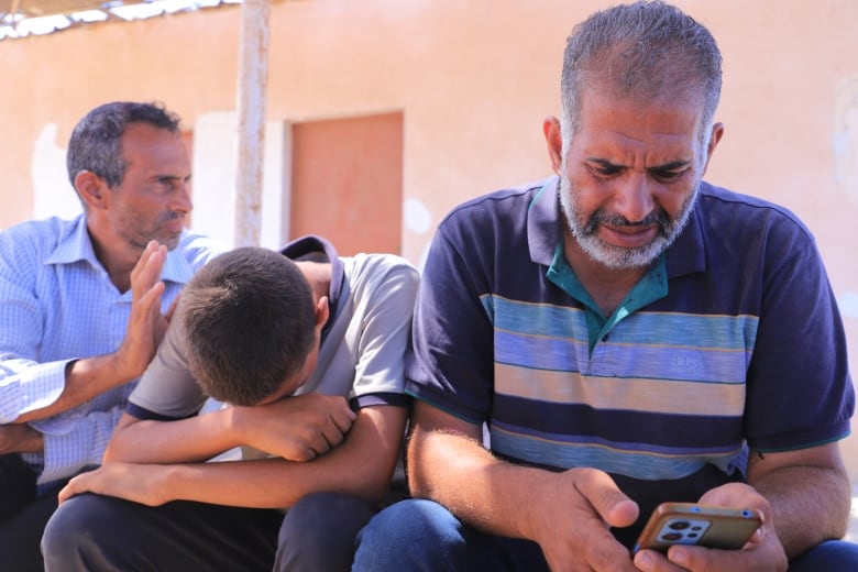 A man in a striped shirt cries as he looks at his phone