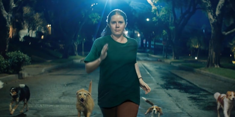 A woman runs down a street at night surrounded by dogs. 