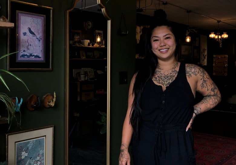 A woman smiles at the camera within her tattoo shop.