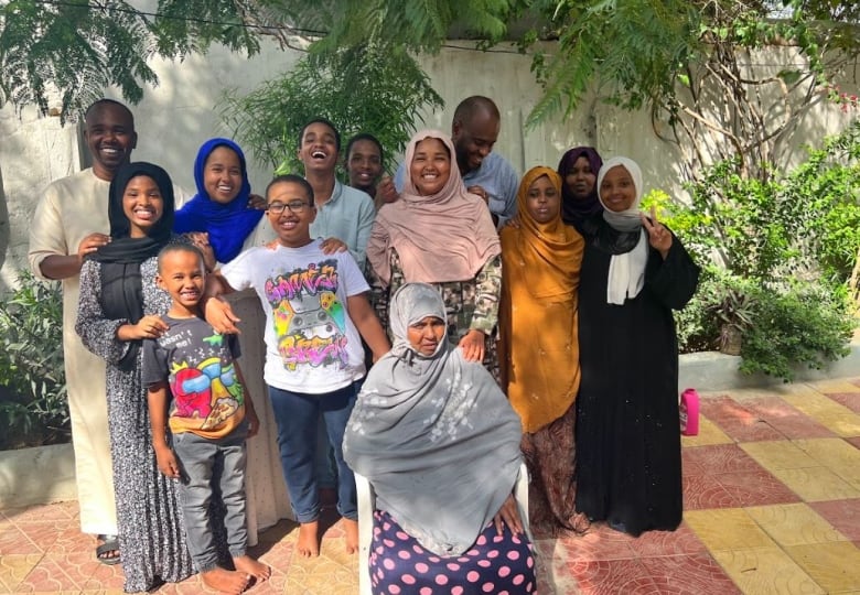 A family with several smiling African men, women and children, standing and sitting.