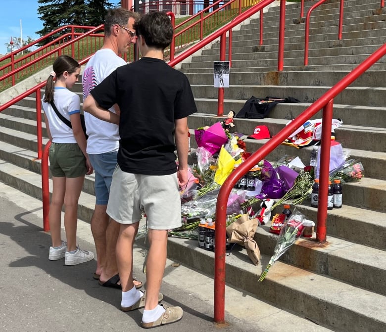 A man, a boy and a girl stand in front of steps adorned with bouquets of flowers.