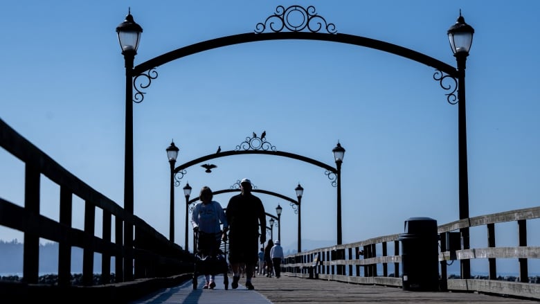 Two people walk along a mat on a pier. 