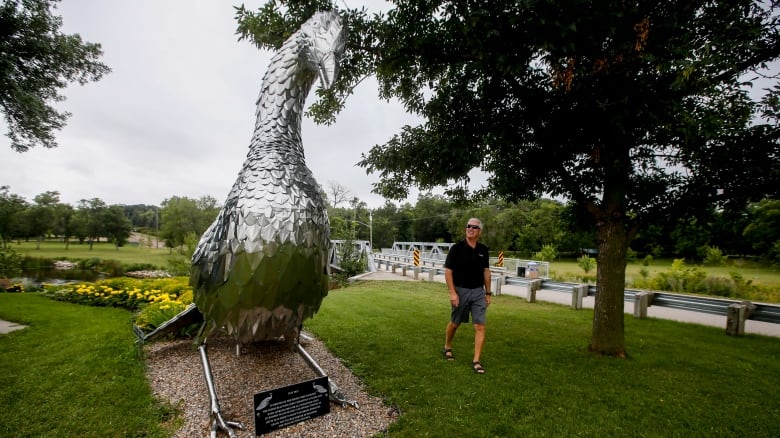 A man walks near a large metal statue of a peacock.