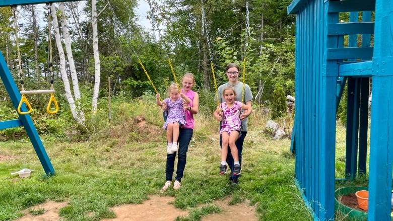 Two teenage girls push two yougner girls on a blue wooden swingset.