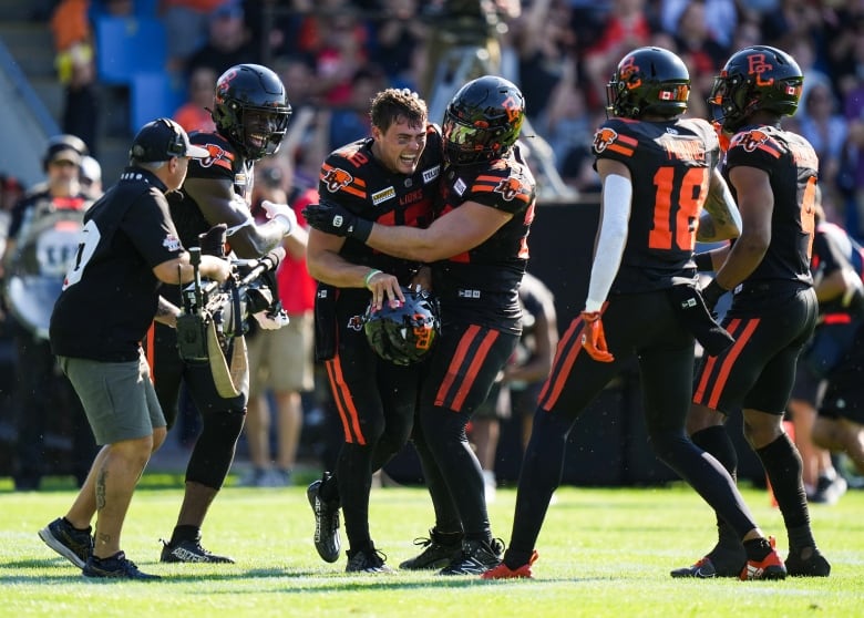 Five players in the field celebrate as a person with a camera films them.