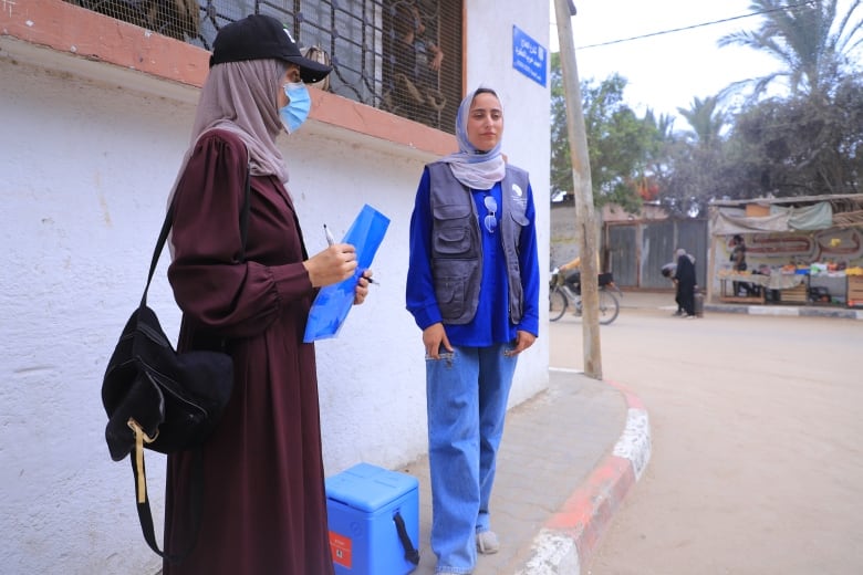 Two women stand on a sidewalk 