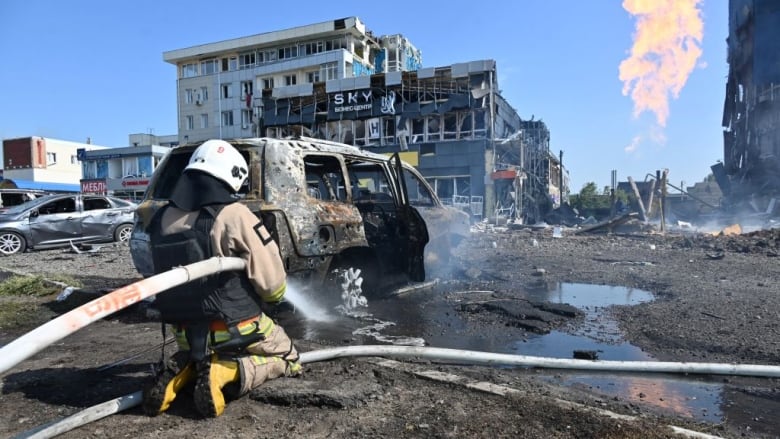 A firefighter kneels on the ground while holding a hose and spraying water.