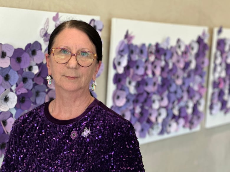 A woman stands by a wall with purple poppies.