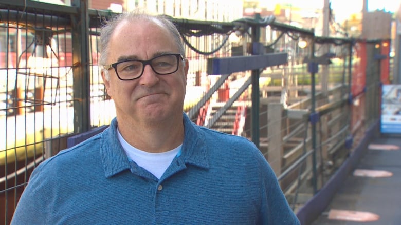 A white man wearing a blue shirt smiles in front of construction equipment.