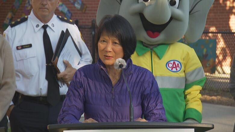 Mayor Olivia Chow stands in front of a podium outside a school.