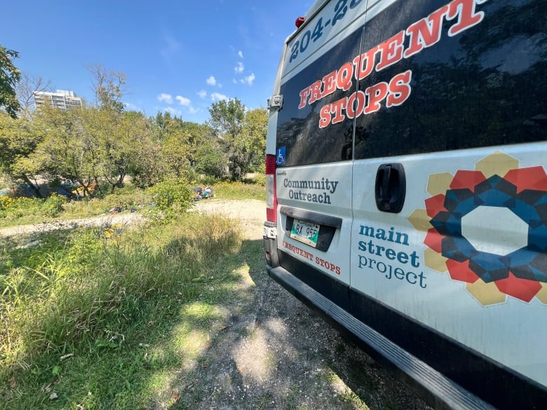 The back doors of a van are seen near a homeless encampment in a park