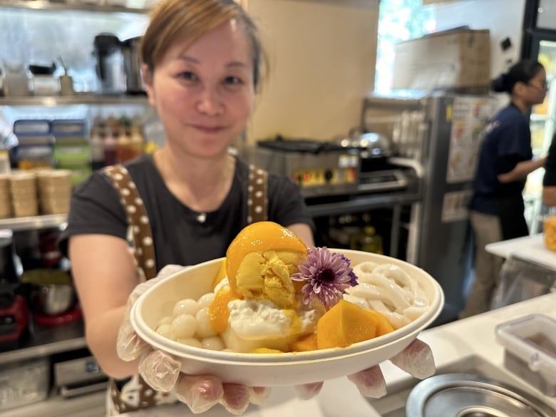 A woman holds a large, fancy dessert with mango syrup, mango ice cream, panacotta, coconut noodles and other tasty things.