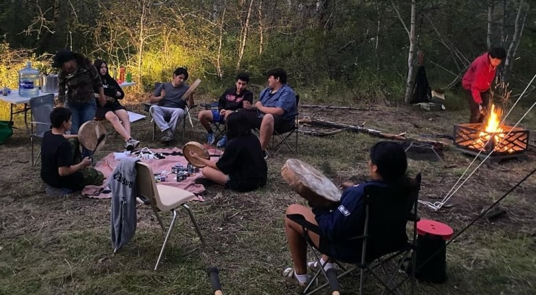 A photo of youth sitting together holding hand drums, and talking. 