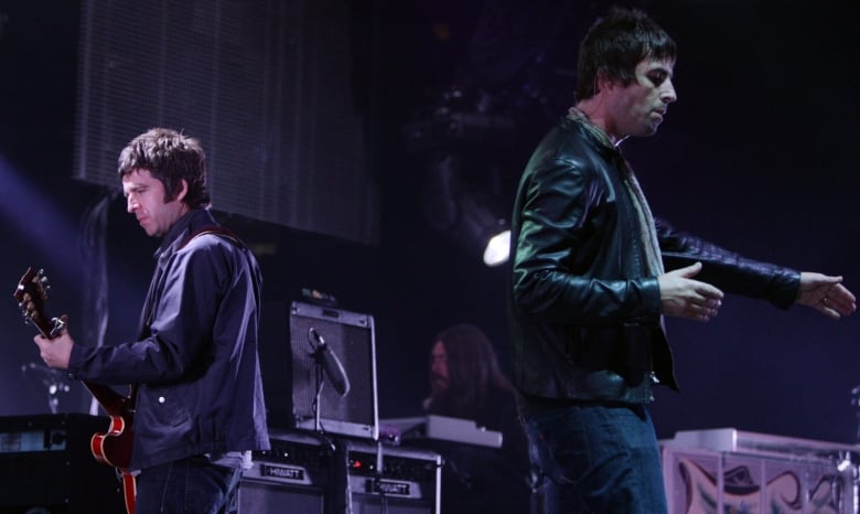 Two men stand on a stage, one holding a guitar. 