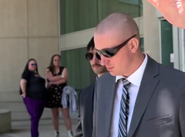 A man in a suit wearing sunglasses leaves a court building.