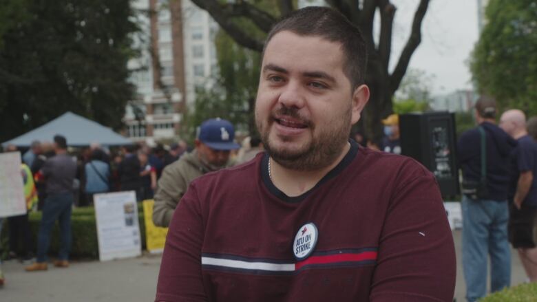 A white man wearing a maroon shirt speaks at a rally.