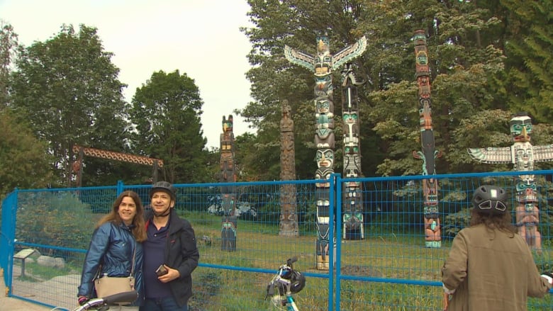 A number of tourists take pictures in front of a series of totem poles.