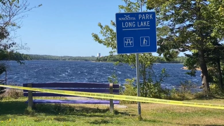 Police tape in front of a purple bench and blue sign.