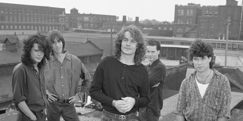 A black and white photo shows the five members of the Tragically Hip posing on a rooftop. 