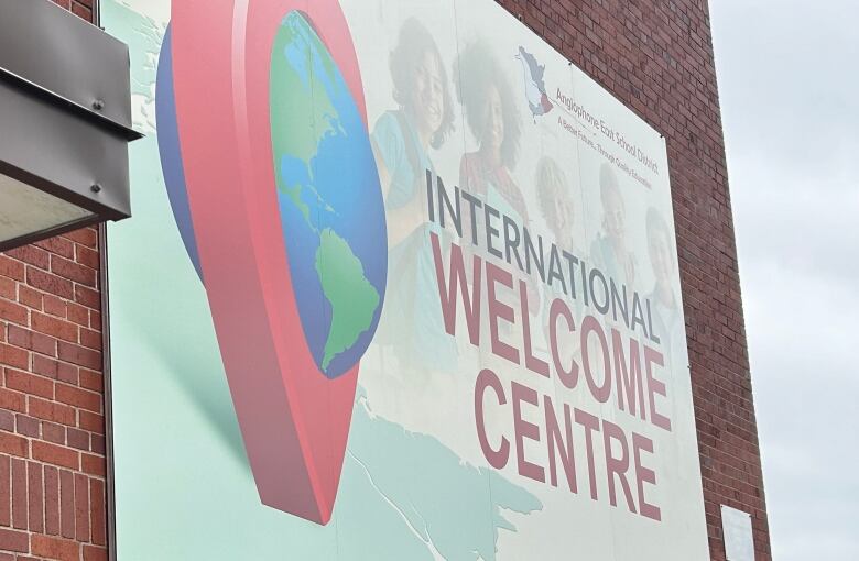 A smiling woman stands outside a brick building that has a huge sign reading 