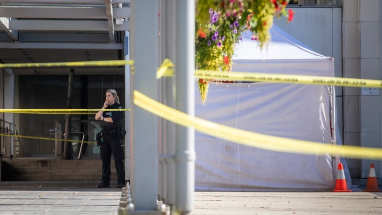 A VPD officer stands next to a white tent and crime scene tape.