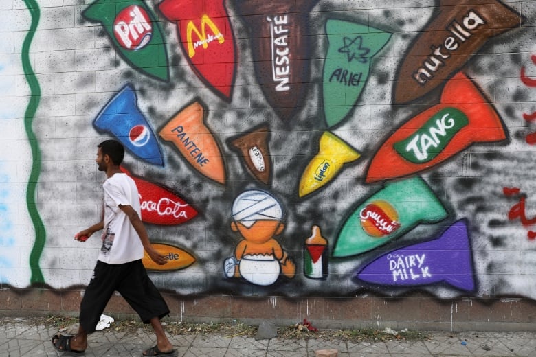 A man walks past a wall covered in graffiti depicting several well-known brands. 