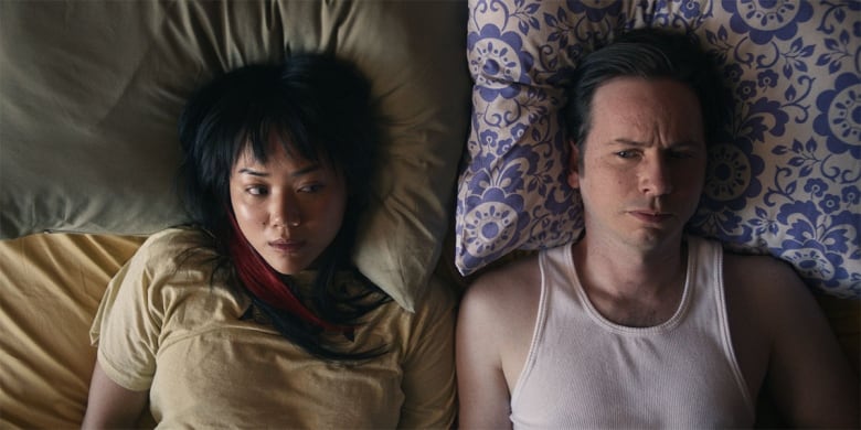 An East Asian woman and a white man lay side-by-die on a bed, close up film still.