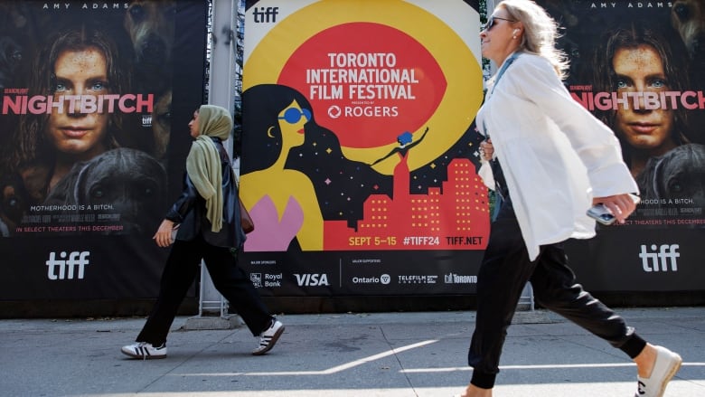 Two women walk past posters for the Toronto International Film Festival.