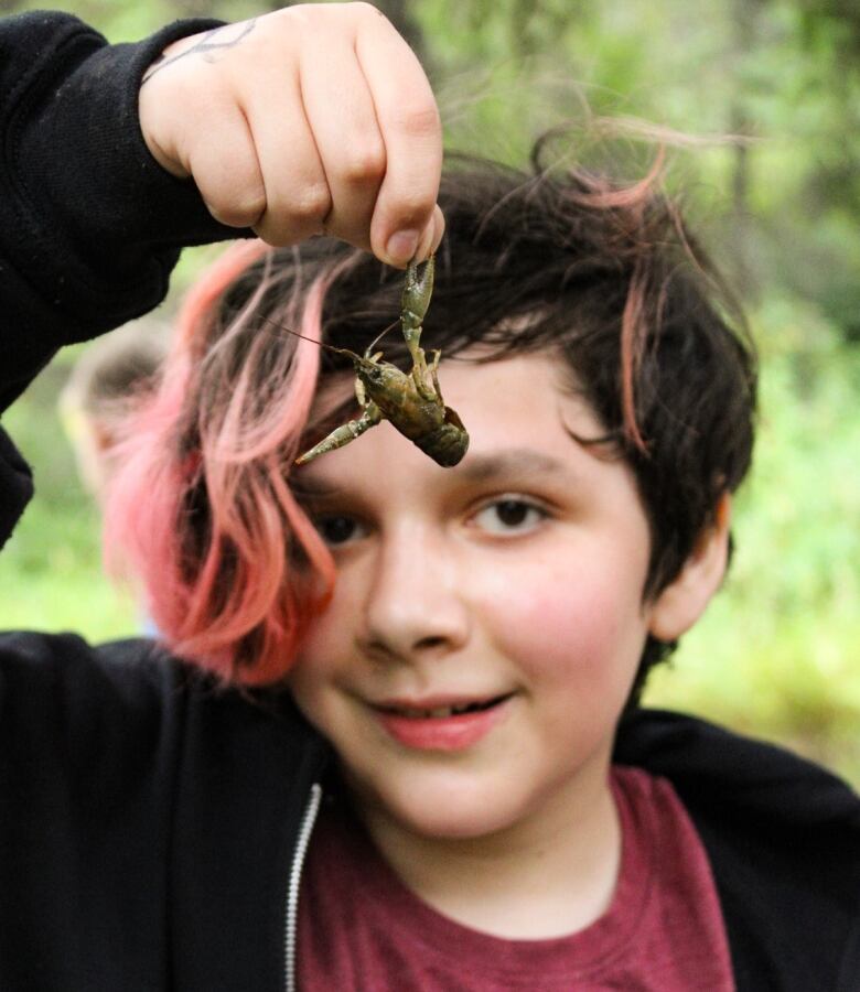 Achild holds an insect and smiles