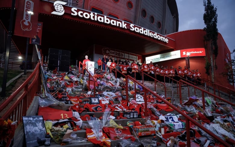 A man stands behind a podium on a set of stairs covered with memorial items. 