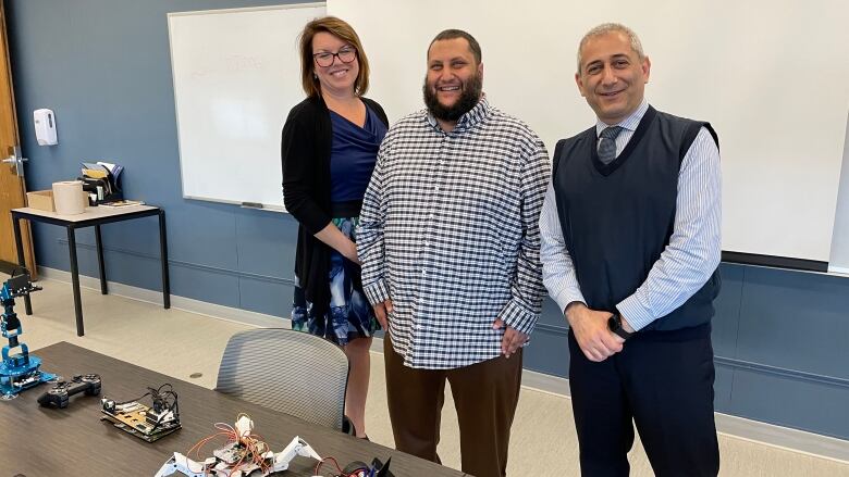 Three people standing in a classroom.