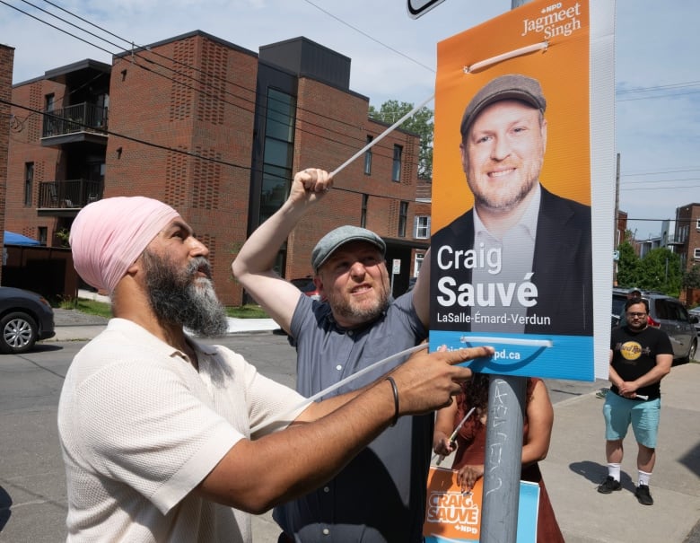 Two men ziptie a electoral campaign sign to a lamp post.