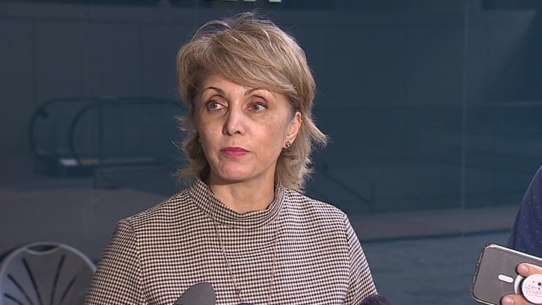 A woman stands in front of a glass wall.