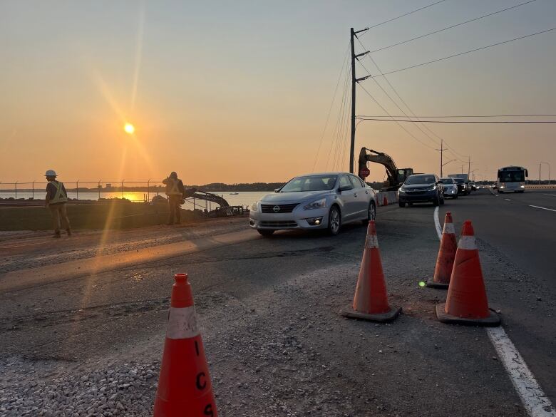 Lineups of cars trying to cross a bridge with construction workers standing in the background.