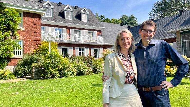 A couple pose for a photo in front of a house.