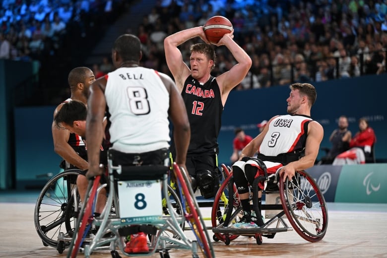 Wheelchair basketball players on the court during a game at the Paralympics, with a packed crowd in the bleachers watching.