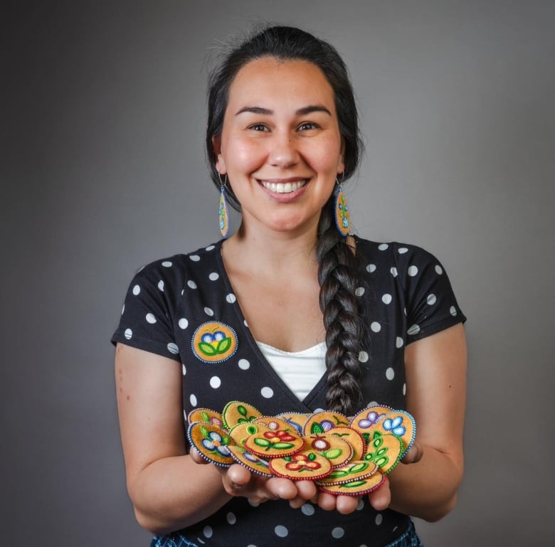 An Indigenous woman smiles as she holds moose hide beaded pins