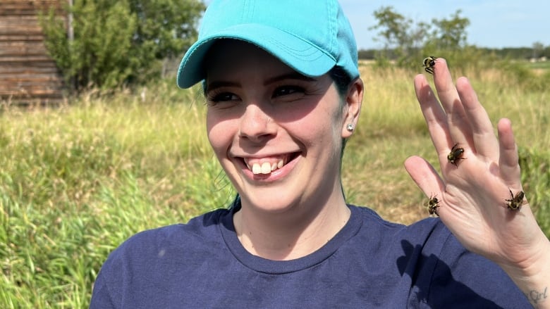 Woman wearing navy blue shirt, and a turquoise hand smiling. She's holding her hand up in the air, there are four bumblebees resting on her hand. 