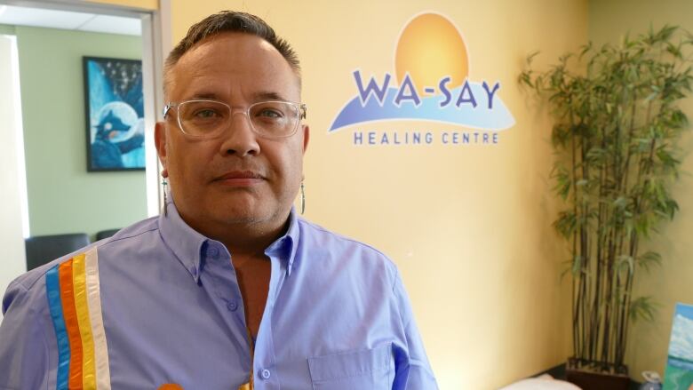 A man standing in front of wall with a logo that says 'Wa-Say Healing Centre'