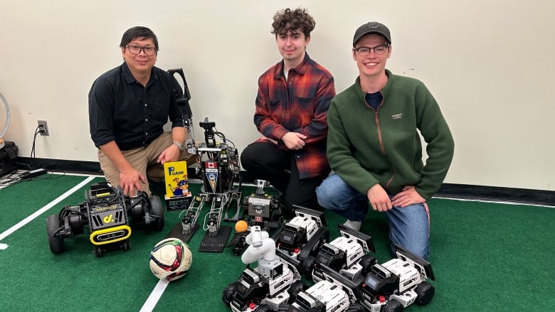 Three people kneeling next to several robots.