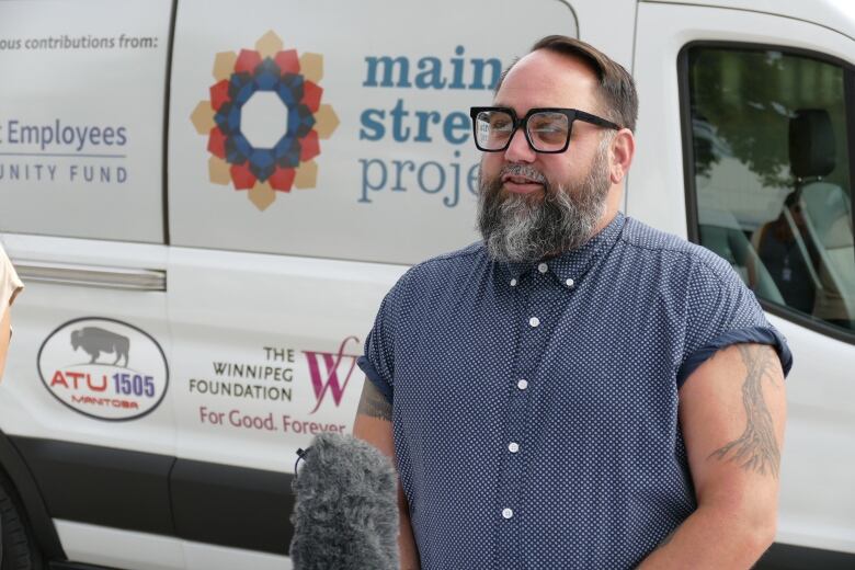 Man stands in front of white van speaking into microphone.